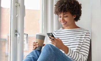 happy dark skinned female with pleased expression reads online book via cell phone checks email social networks min